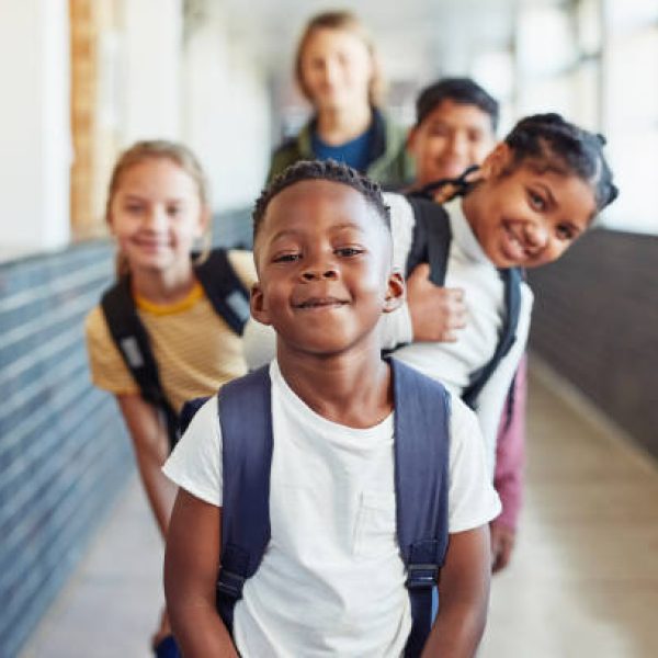istockphoto-1170717275-612×612 Portrait of a group of young children standing in a line in the hallway of a school